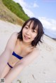 A woman in a blue bikini sitting on a beach.