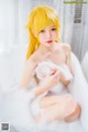 A woman with yellow hair sitting in a bathtub filled with foam.