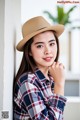 A woman wearing a straw hat leaning against a wall.