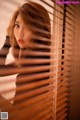 A woman looking out of a window with blinds.