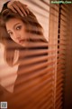 A woman leaning against a window with blinds.