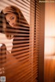 A woman looking out of a window with blinds.