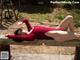 A woman in a red bodysuit laying on a wooden bench.