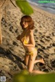 A woman in a yellow bikini sitting on a beach.