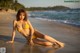 A woman in a yellow bikini sitting on the beach.