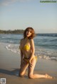 A woman in a yellow bikini sitting on the beach.