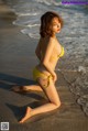 A woman in a yellow bikini sitting on the beach.