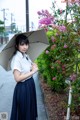 A woman in a white shirt and blue skirt holding an umbrella.