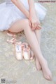 A woman in a white tutu and pointe shoes sitting on the floor.