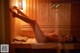 A naked woman laying on a wooden bench in a sauna.