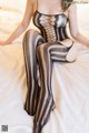 A woman in a black and white striped bodysuit sitting on a bed.