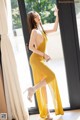 A woman in a yellow dress leaning against a window.