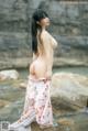 A woman in a white bikini standing on a rock by the water.