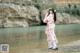 A woman in a pink kimono standing by a river.