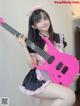 A woman in a maid outfit holding a pink guitar.