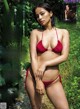 A woman in a red bikini standing in the woods.