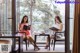 Two women sitting at a table reading a book.