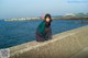 A woman sitting on a concrete wall by the water.