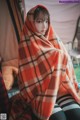 A woman wrapped in a blanket sitting in front of a tent.