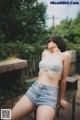 A woman in a white bra top and denim shorts sitting on a bench.