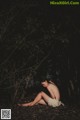 A naked woman sitting on the ground in the woods.