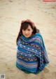 A young girl wrapped in a blanket on the beach.