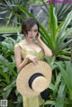 A woman in a yellow dress holding a straw hat.