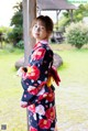 A woman in a kimono standing next to a wooden pole.