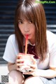 A young woman sitting on the ground drinking a drink.