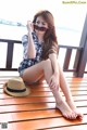 A woman sitting on a wooden deck with a hat and sunglasses.