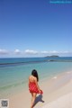 A woman in a red dress walking on a beach.