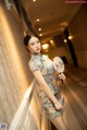 A woman in a cheongsam holding a fan in a hallway.