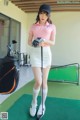 A woman in a pink shirt and white skirt holding a golf club.