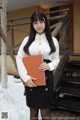 A woman in a white shirt and black skirt holding a book.