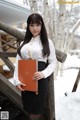 A woman in a white shirt and black skirt holding a book.