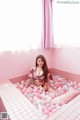 A woman sitting in a bathtub filled with pink and white balloons.