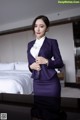 A woman in a purple suit standing in front of a bed.