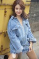 A woman in a denim jacket leaning against a yellow truck.