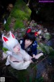 A couple of women sitting on top of a rock next to a stream.