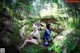 A couple of women sitting on top of a rock in the woods.