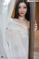 A woman in a white sari leaning against a curtain.