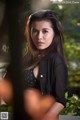 A woman in a black shirt leaning against a tree.