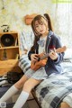 A woman sitting on a bed playing a ukulele.