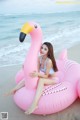 A woman sitting on an inflatable flamingo on the beach.