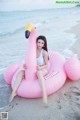 A woman sitting on an inflatable flamingo on the beach.