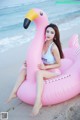 A woman sitting on an inflatable flamingo on the beach.