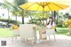 A woman sitting on a chair under an umbrella.