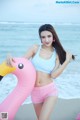 A woman in a bikini holding a pink flamingo on the beach.