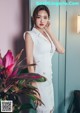 A woman in a white dress standing next to a plant.