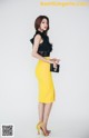 A woman in a yellow skirt and black top posing for a picture.